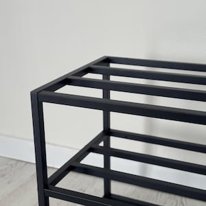 Op de afbeelding: Een zwart metalen schoenenrek met een rechthoekig frame en meerdere horizontale staven voor schoenenopslag. Het rek heeft een minimalistisch ontwerp en is geschikt voor het organiseren van schoenen.
