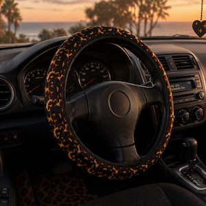 Puede incluir: Interior de coche con volante negro y funda con estampado de leopardo. El salpicadero muestra indicadores, radio y rejillas de ventilación. Un adorno en forma de corazón cuelga del espejo retrovisor. El fondo muestra una puesta de sol sobre el mar.