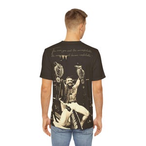 May include: Black t-shirt featuring a sepia-toned image of a man holding championship belts. The image includes the text, "The more you seek the uncomfortable, the more you will become comfortable."