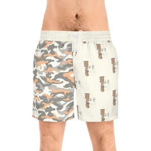 Może przedstawiać: Szorty kąpielowe z podzielonym wzorem. Jedna strona ma wzór kamuflażu w odcieniach szarości, bieli i brzoskwini. Druga strona ma kremowe tło z powtarzającymi się grafikami czaszek i słowem "END". Szorty mają talię ze sznurkiem.