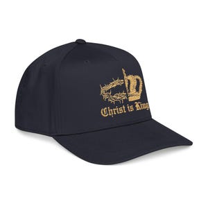 Op de afbeelding: Marineblauwe baseballcap met gouden borduursel. Het ontwerp omvat een kroon, een doornenkroon en de tekst "Christ is King". De cap heeft een gebogen klep en een gestructureerde pasvorm.