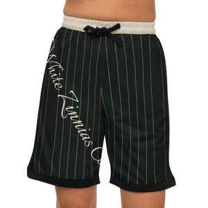 May include: Black athletic shorts with white vertical pinstripes. The shorts have a cream-colored waistband with a black drawstring and a black hem. The words "Tate Finnias" are written in a cursive font on the left leg.