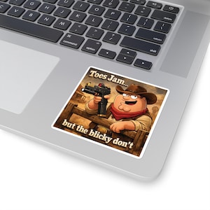 May include: A sticker featuring a cartoon cowboy holding a gun, with the text "Toes Jam... but the blicky don't." The cowboy is wearing a brown hat, red scarf, and a tan vest. The background depicts a western scene.