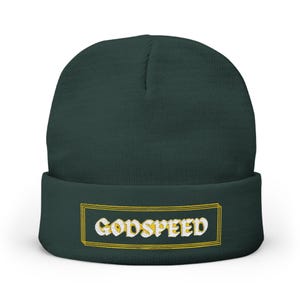 May include: A dark green beanie with the word "GODSPEED" embroidered in white and yellow. The text is inside a yellow rectangular border. The beanie is made of a soft, knitted material.