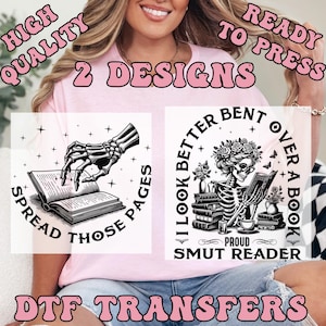May include: Pink t-shirt with two black and white DTF transfer designs. One design features a skeleton hand reaching for an open book with the text "Spread Those Pages." The other design shows a skeleton reading a book with the text "I Look Better Bent Over A Book, Proud Smut Reader."