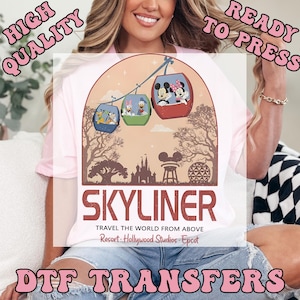 May include: Pink t-shirt featuring a graphic of the Skyliner gondolas with Mickey and Minnie Mouse, Donald and Daisy Duck, and Goofy and Pluto. The text "SKYLINER" and "TRAVEL THE WORLD FROM ABOVE" are also included. The words "DTF TRANSFERS" are at the bottom.