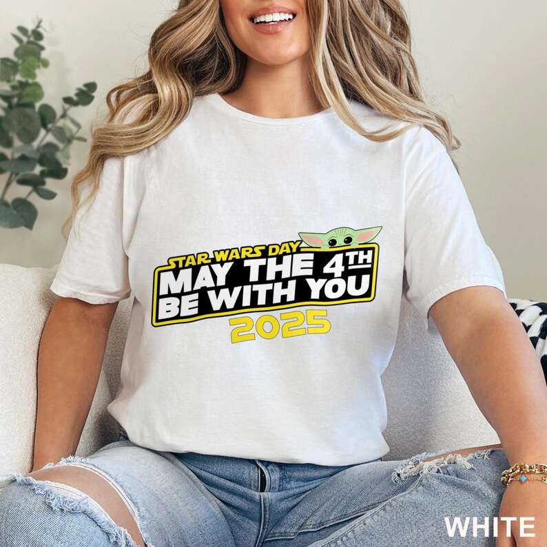 Puede incluir: Camiseta blanca con un dise&ntilde;o del D&iacute;a de Star Wars. El dise&ntilde;o incluye el texto "STAR WARS DAY MAY THE 4TH BE WITH YOU 2025" en amarillo y negro, con una ilustraci&oacute;n de Baby Yoda verde.