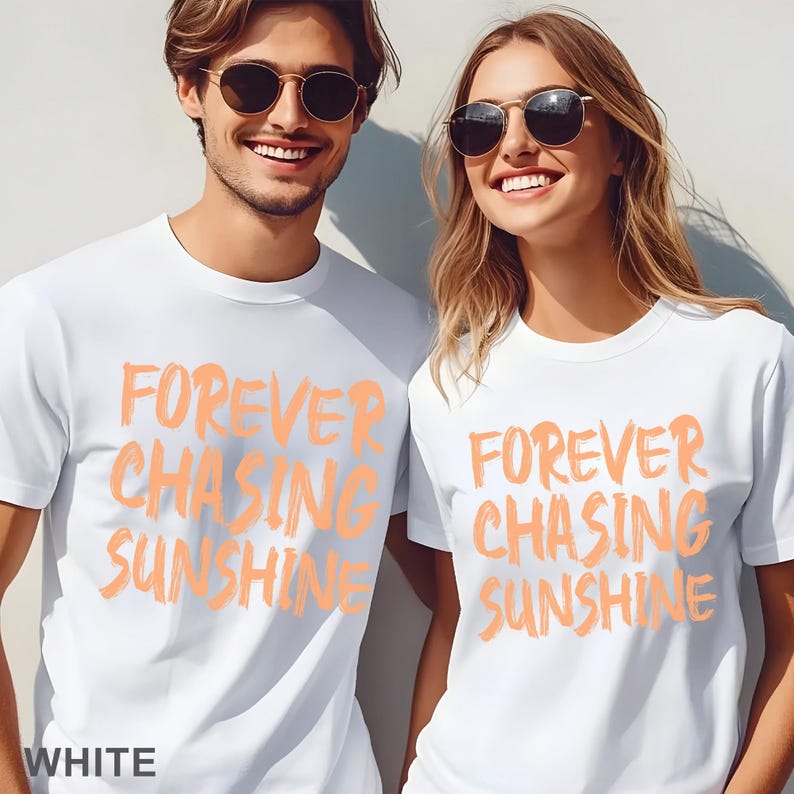 May include: Two white crew neck t-shirts featuring the text FOREVER CHASING SUNSHINE printed in a light orange brushstroke font. The shirts have short sleeves and a standard fit. The word WHITE is printed in the bottom left corner of the image.