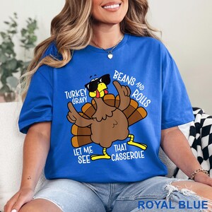 Puede incluir: Camiseta azul real con un pavo de dibujos animados con gafas de sol y gesticulando con las alas. El texto de la camiseta dice: "Turkey Gravy, Beans and Rolls, Let Me See That Casserole."