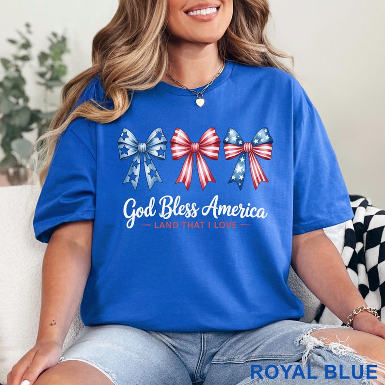 May include: Royal blue t-shirt featuring three patriotic bow designs in red, white, and blue. The text "God Bless America - LAND THAT I LOVE" is printed below the bows. The shirt is a comfortable, casual style.