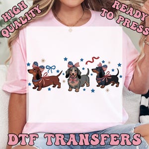 May include: DTF transfers featuring three dachshunds with patriotic bows and ribbons, surrounded by stars. The text "HIGH QUALITY READY TO PRESS DTF TRANSFERS" is displayed in a pink, retro font.