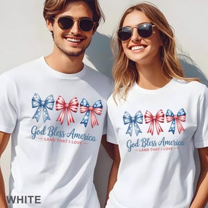 May include: White t-shirts with a patriotic design. The shirts feature three bow illustrations in red, white, and blue, with the text "God Bless America - Land That I Love." The word "WHITE" is at the bottom of the image.