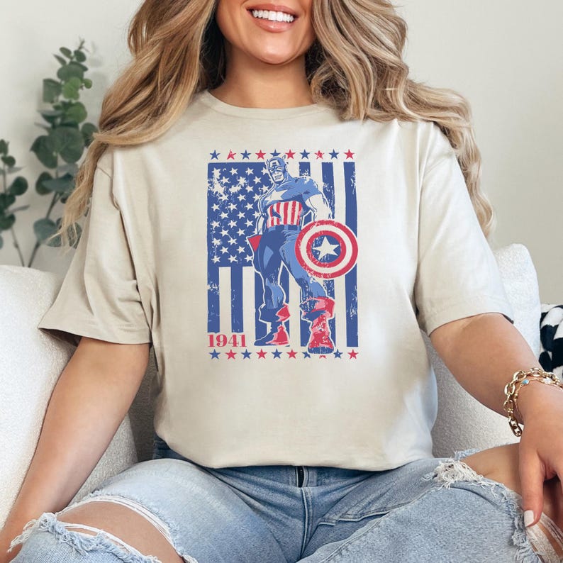 May include: Beige t-shirt featuring a distressed graphic of Captain America with his shield, standing in front of a blue and red American flag design. The year "1941" is printed below the graphic.