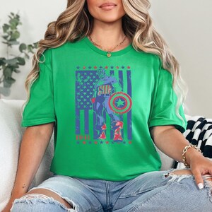 May include: A green t-shirt featuring a graphic of Captain America in front of a distressed American flag design. The graphic includes the text "1941" in red. The shirt is worn by a person.