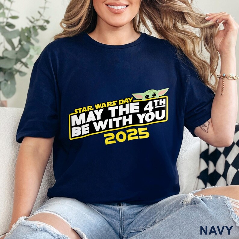 Puede incluir: Camiseta azul marino con un dise&ntilde;o del D&iacute;a de Star Wars. El dise&ntilde;o incluye el texto "STAR WARS DAY MAY THE 4TH BE WITH YOU 2025" en blanco y amarillo, junto con una ilustraci&oacute;n verde de Baby Yoda.