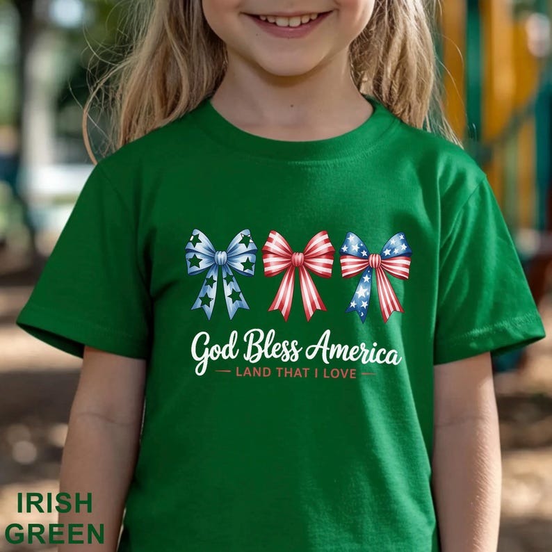 May include: Irish green t-shirt featuring three decorative bows in red, white, and blue, with the text "God Bless America - Land That I Love." The bows have star and stripe patterns.