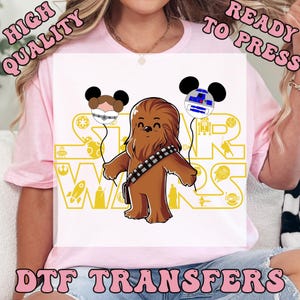 May include: A white DTF transfer featuring a cartoon Chewbacca character holding two Mickey Mouse-shaped balloons, one with Princess Leia and the other with R2-D2. The Star Wars logo is in gold. Text reads "HIGH QUALITY READY TO PRESS DTF TRANSFERS."