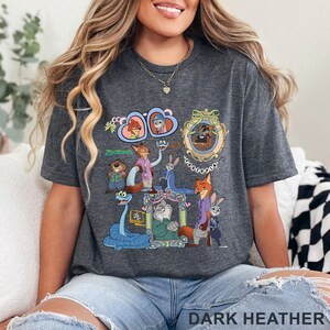 May include: Dark heather gray t-shirt featuring a colorful graphic of characters from the animated movie "Zootopia." The design includes various animal characters in detailed frames and the word "Zootopia."