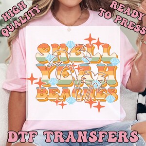 May include: A white DTF transfer with the text "Shell Yeah Beaches" in orange, yellow, and green retro font. The design includes palm trees, seashells, and starbursts. The words "High Quality" and "Ready to Press" are also visible.