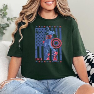 May include: Dark green t-shirt featuring a graphic of Captain America with a shield, standing in front of a distressed American flag. The year "1941" is printed below the flag in red and blue stars.