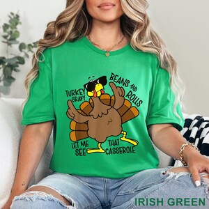 Puede incluir: Una camiseta verde con un pavo de dibujos animados con gafas de sol y el texto "Turkey Gravy, Beans and Rolls, Let Me See That Casserole." La camiseta es de color "Verde Irland&eacute;s".