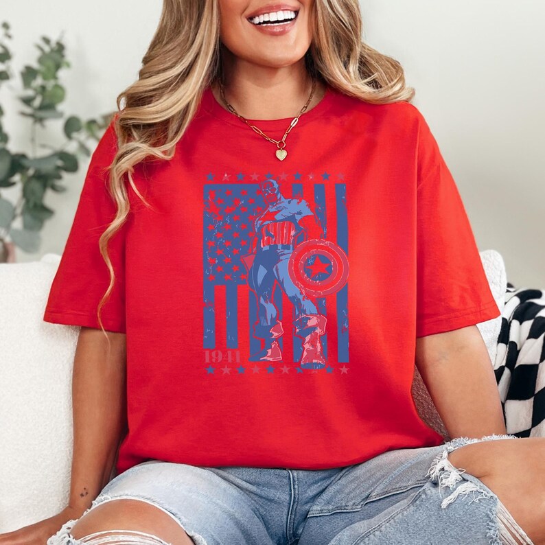 May include: Red t-shirt featuring a distressed graphic of Captain America holding his shield in front of an American flag design. The year "1941" is printed below the flag. The shirt is a casual, oversized fit.