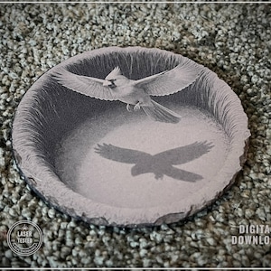 May include: A grayscale image of a round, stone-like coaster featuring a bird in flight with its shadow below. The coaster has a rough, textured edge. The words "LASER TESTED" and "DIGITAL DOWNLOAD" are visible.