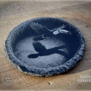 May include: A dark blue, round, stone coaster with a laser-etched image of a toucan in flight. The coaster has a rough, textured edge and a shadow of the bird is visible. The words "DIGITAL DOWNLOAD" are printed on the right side.