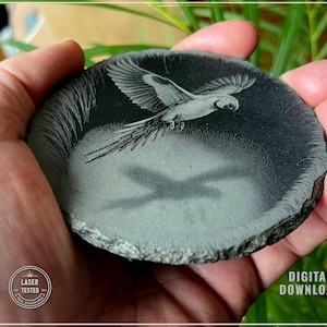May include: A round, dark gray stone with a laser-etched design of a parrot in flight. The parrot's shadow is also visible. The stone has a rough, natural edge. The words "DIGITAL DOWNLOAD" are in the image.