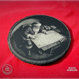 May include: A circular black slate coaster featuring a laser-engraved illustration of Santa Claus sitting at a desk and examining a large map. The design includes gift boxes on the desk. The text LASER TESTED and DIGITAL DOWNLOAD is visible.