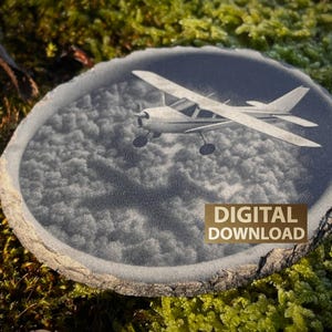 May include: A circular wooden art piece with a detailed engraving of a small airplane flying above a cloudscape. The words "DIGITAL DOWNLOAD" are printed in a gold color on the bottom right. The piece is set against a background of green moss.