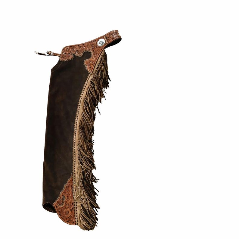 Op de afbeelding: Een donkerbruine leren chap met een beige leren juk en onderpaneel voorzien van gedetailleerd bloemmotief. De zijkant van het been is versierd met lange, beige franjes en een zilverkleurig concho-detail op de tailleband.