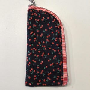 May include: A zippered pouch with a black background and a pattern of red cherries. The pouch has a red and white striped border and a silver zipper pull. The pouch is approximately 7 inches long.