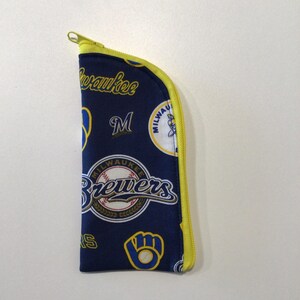 May include: A navy blue zippered pouch featuring the Milwaukee Brewers baseball team logo and wordmark. The pouch has a yellow zipper and trim. The design includes the team's logo, the letter "M", and the word "Brewers".