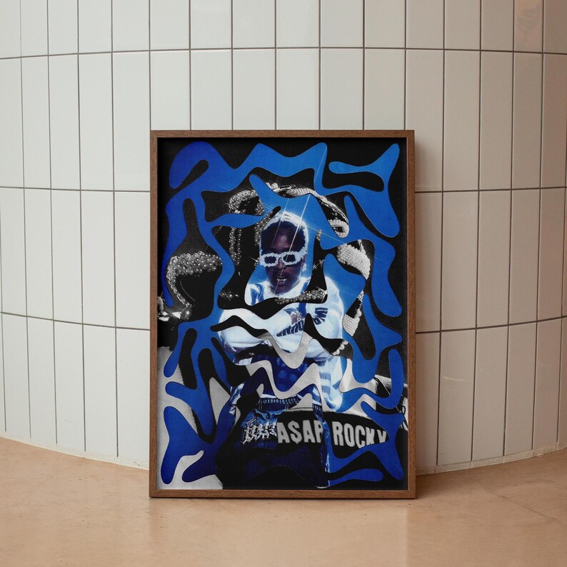 Op de afbeelding: Een ingelijste kunstdruk met een portret van een persoon met een zonnebril, overlegd met blauwe abstracte vormen. De print heeft de tekst "ASAP ROCKY" onderaan. De lijst is donkerbruin.