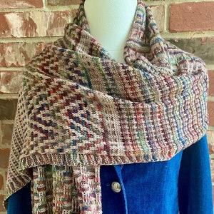 May include: A brown, beige and blue patterned knitted scarf draped over a blue blazer. The scarf has a geometric design.