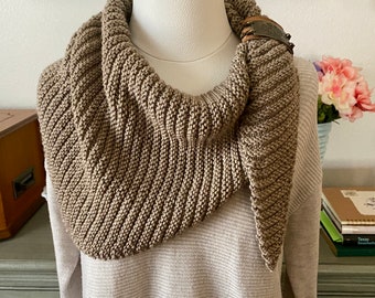 May include: A brown knitted cowl neck scarf with a decorative metal buckle. The scarf is displayed on a white mannequin.