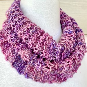 May include: A purple and pink knitted infinity scarf. The scarf is made with a soft, textured yarn and is perfect for keeping warm in the winter.