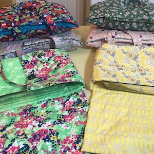 Puede incluir: Una colección de portadores de cazuelas acolchados y manoplas a juego con varios estampados florales y geométricos. Los portadores tienen asas y cierres de botón. Los colores incluyen verde, amarillo, azul, rosa y morado.