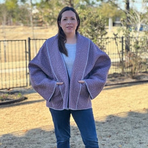 May include: A woman wearing a purple quilted jacket with a shawl collar and blue jeans.