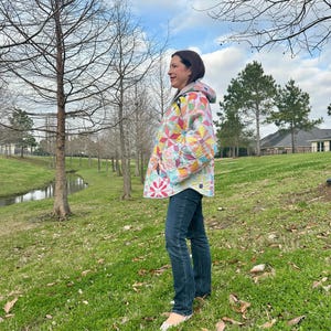 Può includere: Una giacca con cappuccio realizzata con un patchwork multicolore caratterizzato da motivi a stella e floreali nelle tonalità del rosa, giallo, blu e verde, abbinata a jeans blu scuro e scarpe senza lacci di colore chiaro.