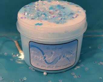 May include: A light blue container of slime labeled "Frosted Waves" with a blue and white design. The slime is topped with blue and white sprinkles and small decorative pieces. The text "Do not eat" is also visible.