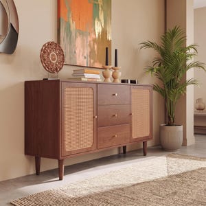 May include: A rectangular wooden sideboard featuring two side cabinets with light-colored woven cane panels and three central drawers with small gold-toned knobs. The furniture piece is supported by four tapered wooden legs and has a smooth finish.