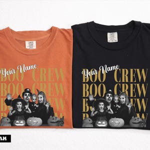 K&ouml;nnte beinhalten: Zwei Rundhals-T-Shirts, eines in Orange und eines in Schwarz, mit dem Text "Your Name" und "BOO CREW" in einem sich wiederholenden Rastermuster. Unter dem Text befindet sich ein Schwarz-Wei&szlig;-Foto einer Familie in Halloween-Kost&uuml;men mit K&uuml;rbissen.