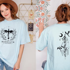 A woman wearing a light blue t-shirt with a graphic design and text, posing in front of a floral background.