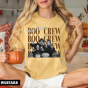 K&ouml;nnte beinhalten: Ein senfgelbes Kurzarm-T-Shirt mit einer schwarz-wei&szlig;en Grafik einer Familie in Halloween-Kost&uuml;men mit K&uuml;rbissen. Der Text lautet "Your Name" in Schreibschrift und "BOO CREW" in gro&szlig;en Blockbuchstaben, die sich im Design wiederholen.