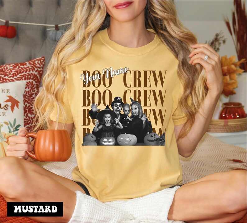 K&ouml;nnte beinhalten: Ein senfgelbes Kurzarm-T-Shirt mit einer schwarz-wei&szlig;en Grafik einer Familie in Halloween-Kost&uuml;men mit K&uuml;rbissen. Der Text lautet "Your Name" in Schreibschrift und "BOO CREW" in gro&szlig;en Blockbuchstaben, die sich im Design wiederholen.
