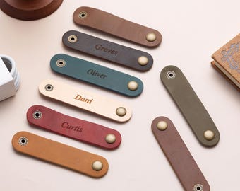 May include: A collection of leather keychains in various colors, including brown, green, and red. Each keychain has a metal snap and is engraved with a name. The names include "Groves", "Oliver", "Dani", and "Curtis".