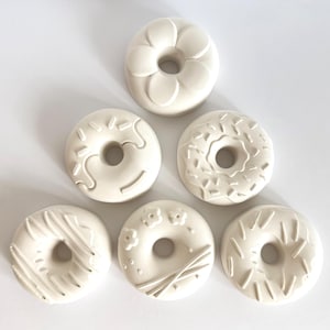 Könnte beinhalten: Ein Set aus drei Keramikbechern mit gesprenkelter, matter Oberfläche. Die Becher sind in Creme-, Hellgrau- und Dunkelgrautönen gehalten. Jeder Becher hat ein schlichtes, minimalistisches Design und einen abgerundeten Henkel. Die Becher sind aufeinander gestapelt.