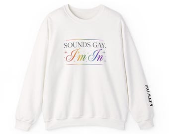 May include: A white long-sleeve sweatshirt featuring the black text SOUNDS GAY. and the multicolored text I'm In with small star accents on the chest. The left sleeve includes the black text MTKOV printed vertically near the cuff.